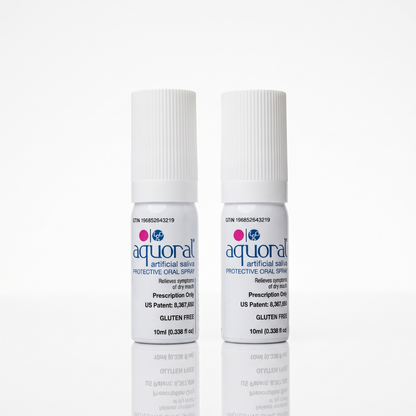 Two small white bottles of aqural artificial saliva protective oral spray standing upright on a white reflective surface.