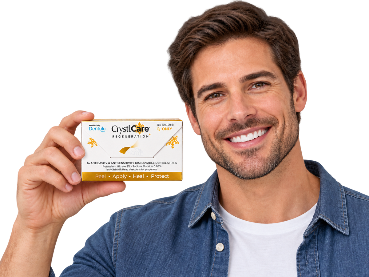 A smiling man in a denim shirt holds up a box of Dentally CrystCare Egeneration + on a clean white background.